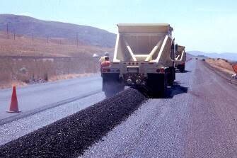 Semi belly-dump trailer releasing aggregate through open bottom gates into a windrow